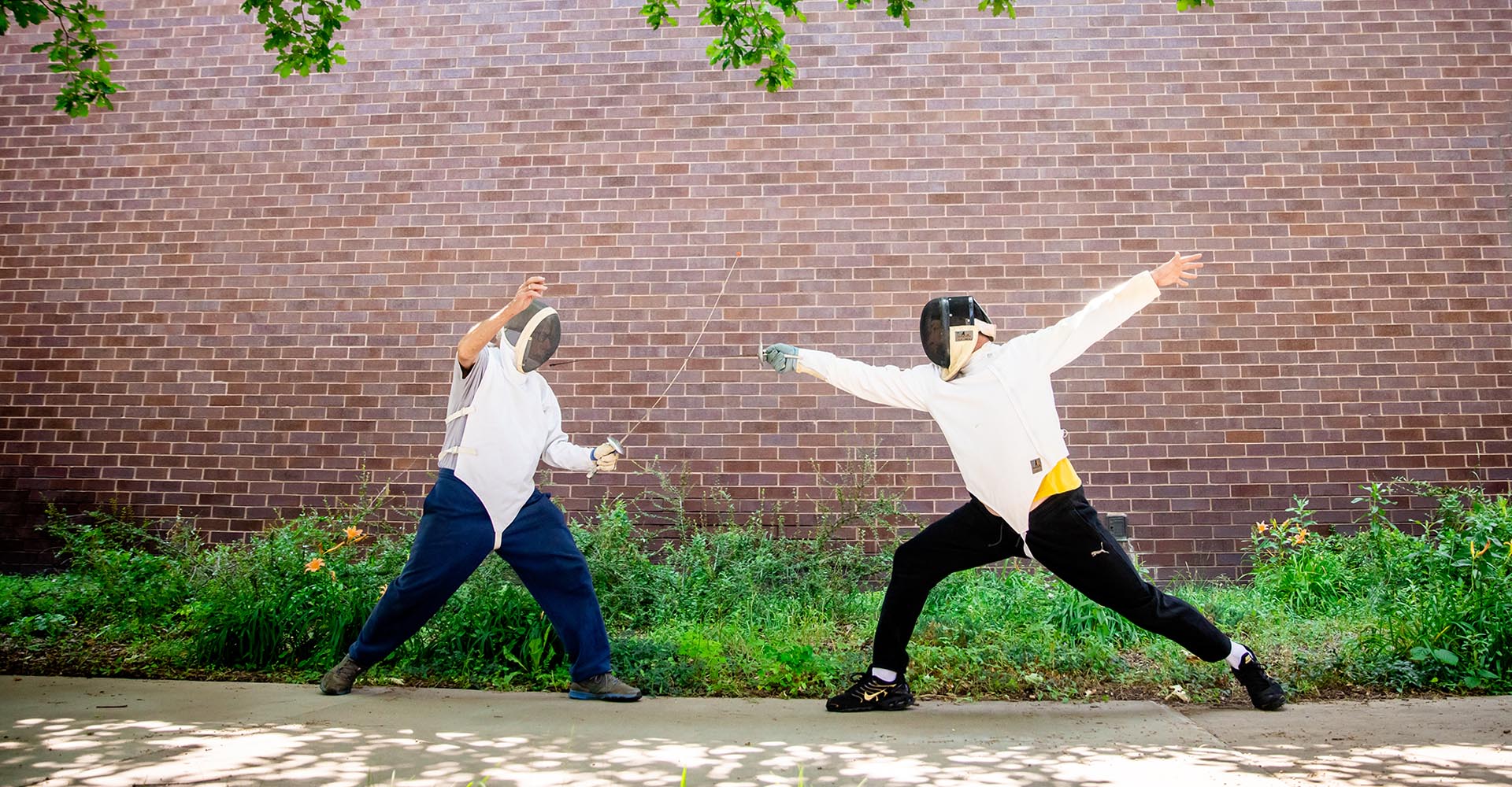 Photo of students fencing against a brick wall