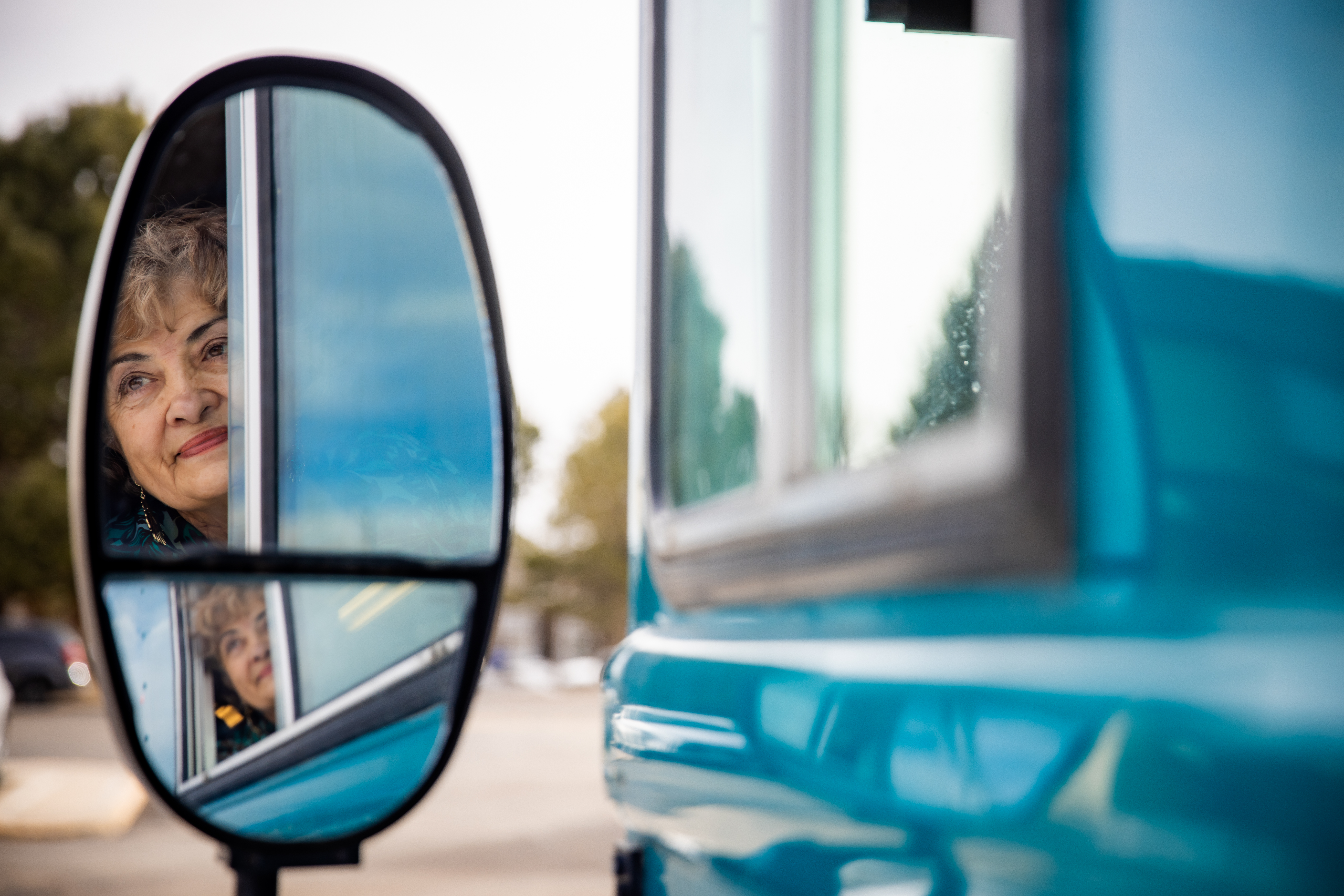 Photo of Roya Brown in the side mirror of her mobile schoolbus