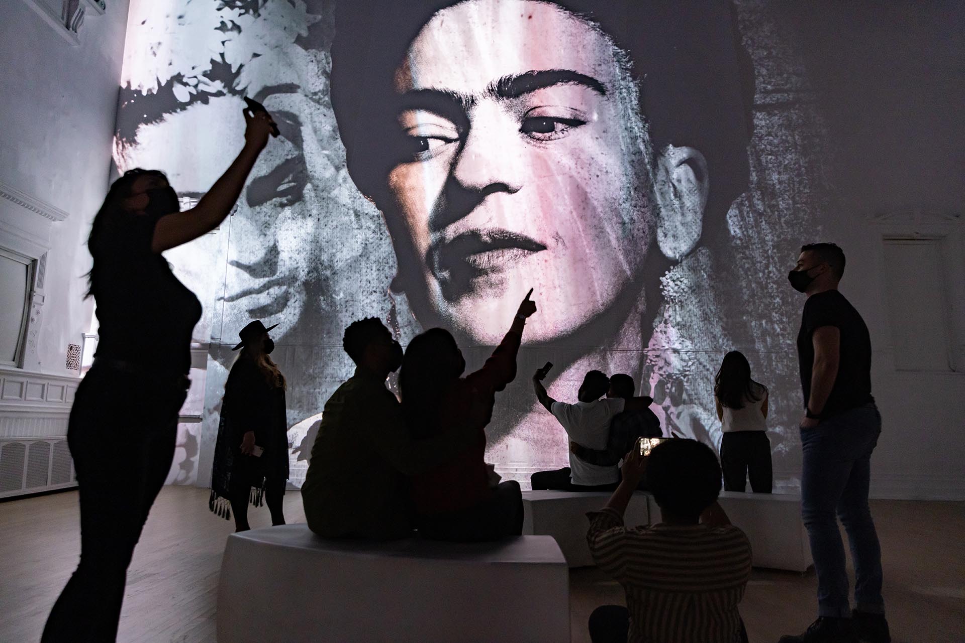 Photo from the Immersive Frida Kahlo exhibition showing Kahlo's image projected on the wall and spectator silhouettes in the foreground