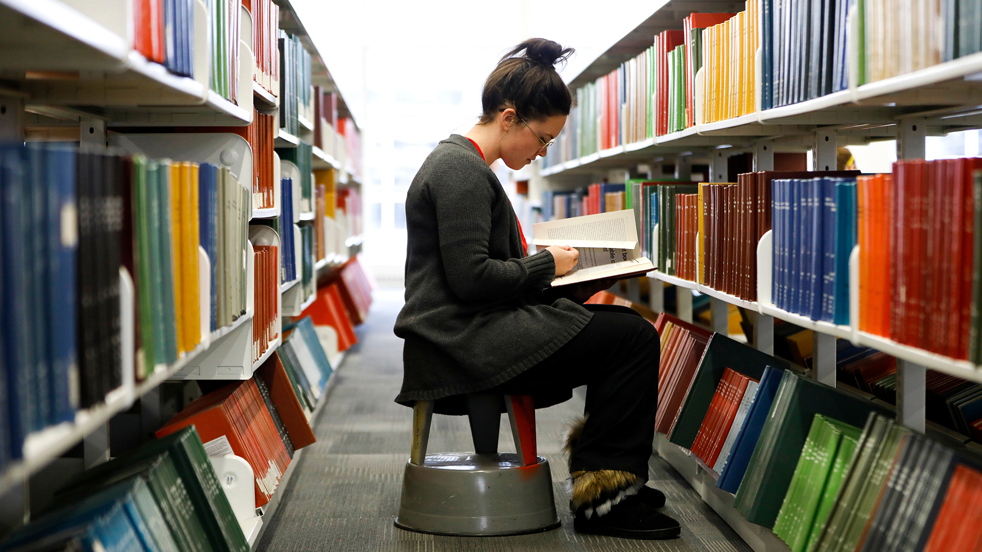 Student reads a book among the shelves at the Auraria Library