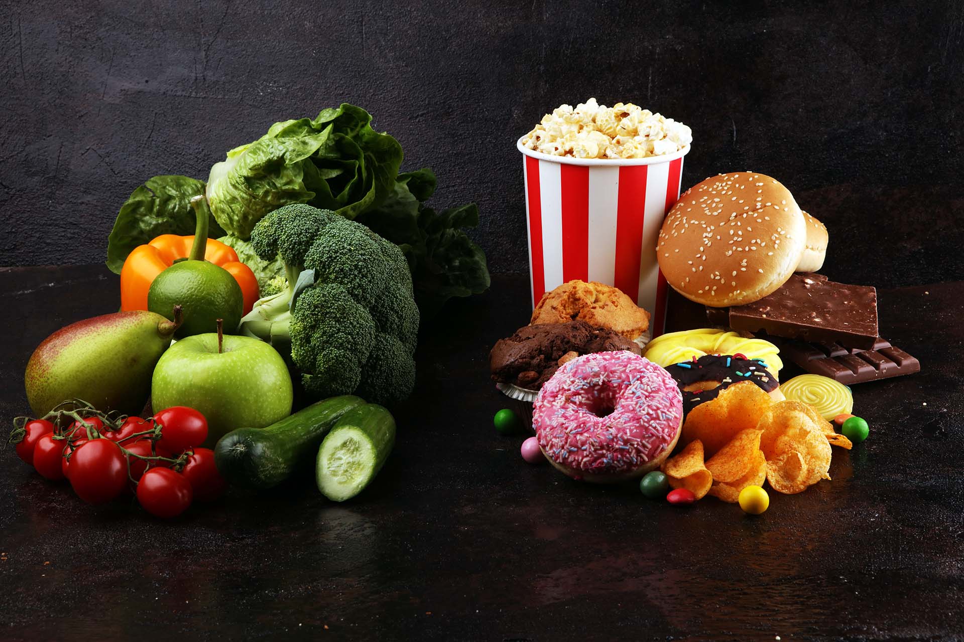 Concept photo of healthy and unhealthy food. Fruits and vegetables vs donuts,sweets and burgers on dark