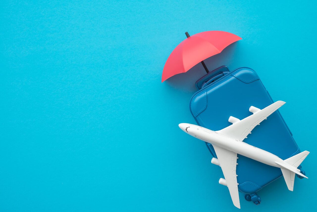 Travel insurance business concept. Red umbrella cover airplane and suitcases on blue background. Travel insurance covers loss suitcase, flight delays, cancellations, accident and medical expenses.