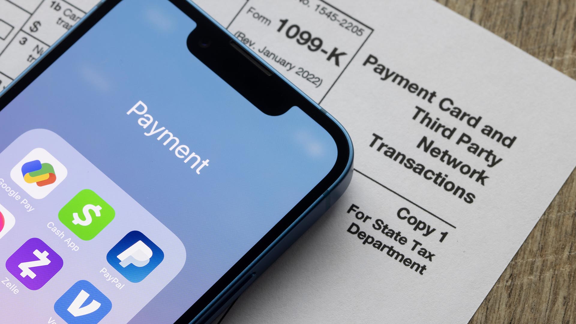 Payment apps like PayPal and Venmo are seen on an iPhone on top of Form 1099-k. Third-party payment apps now have to report transactions more than USD600 to the IRS.