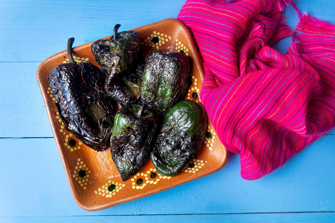 Roasted poblano peppers ready to be peeled in clay plate on colorful backgrounds