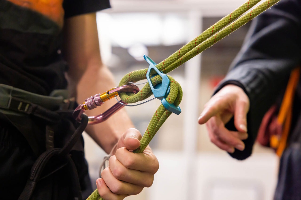 wo individuals attaching a green climbing rope to a blue belay device.