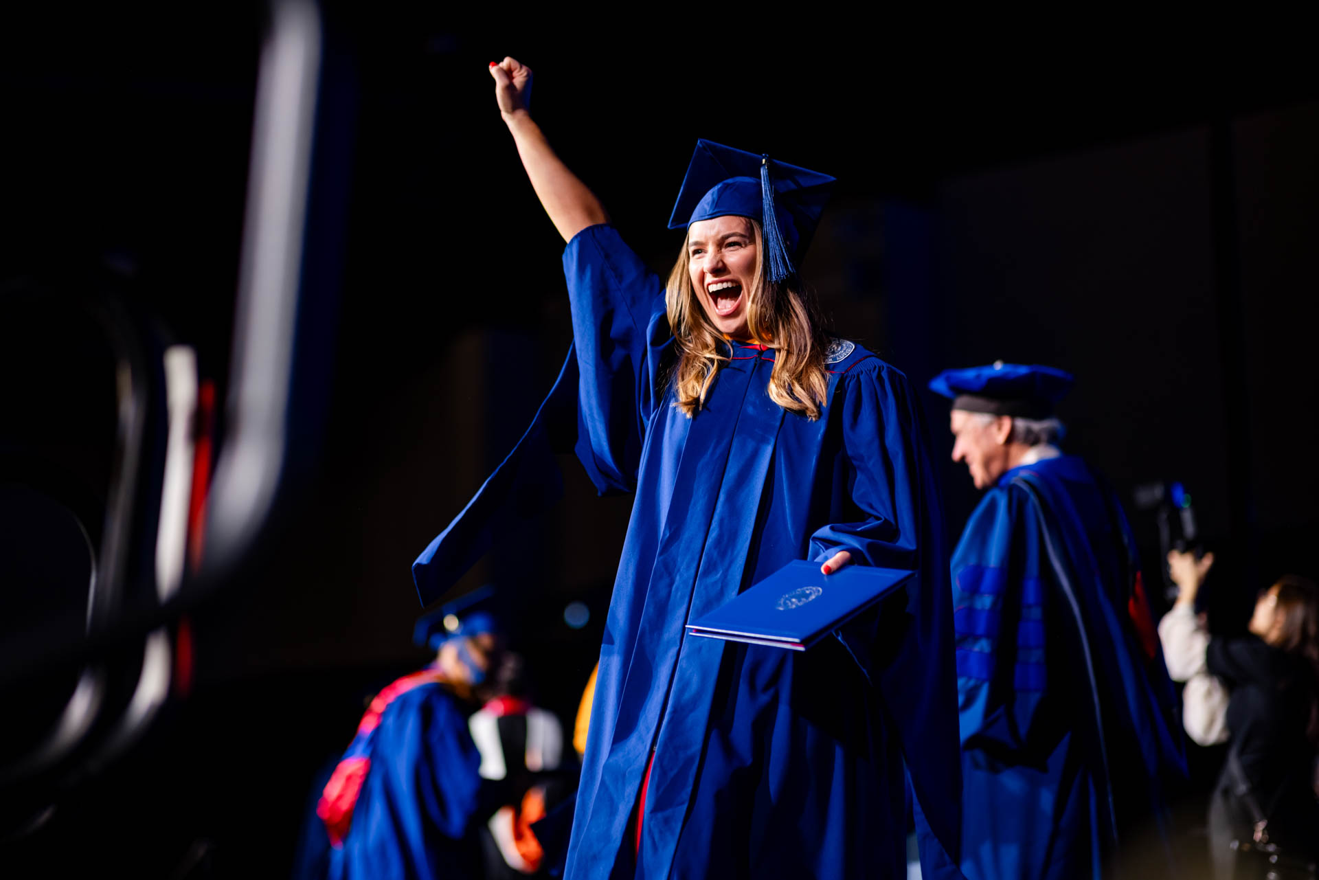 A graduate celebrates with hand in the air after receiving her degree.